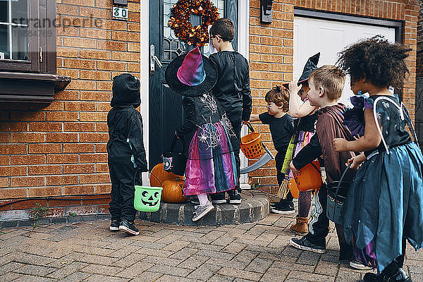 Eine Gruppe von Kindern  die sich zu Halloween an einer Haustür mit Eimern Trick oder Treating verkleidet haben.