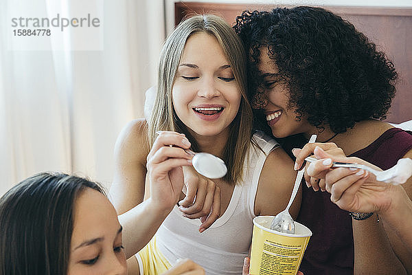 Drei Frauen essen aus Eisbechern und lachen.