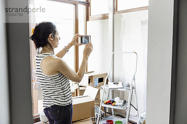Eine Frau  die mit ihrem Mobiltelefon ein Foto macht  mit einer Trittleiter und Pappkartons im Raum.