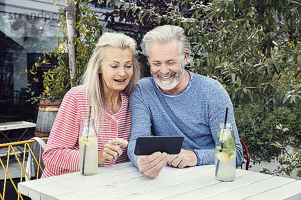 Ein Paar sitzt an einem Tisch in einem Garten mit Flaschengetränken und schaut gemeinsam auf ein Mobiltelefon.