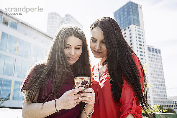 Zwei Frauen stehen in einer Berliner Straße und schauen auf ein Mobiltelefon.