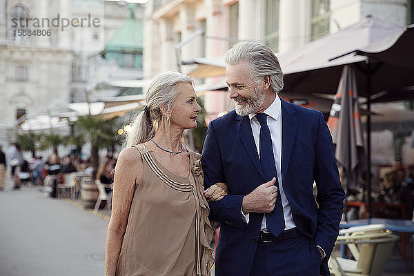 Ein Ehepaar geht Arm in Arm eine Straße mit Bars und Marktständen in Wien entlang.