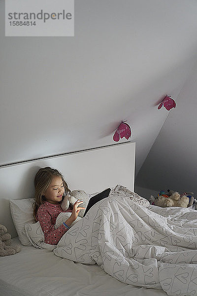 Privatleben  ein Schulvormittag während des Einschlusses. Ein Mädchen liegt im Bett und benutzt ein digitales Tablet.