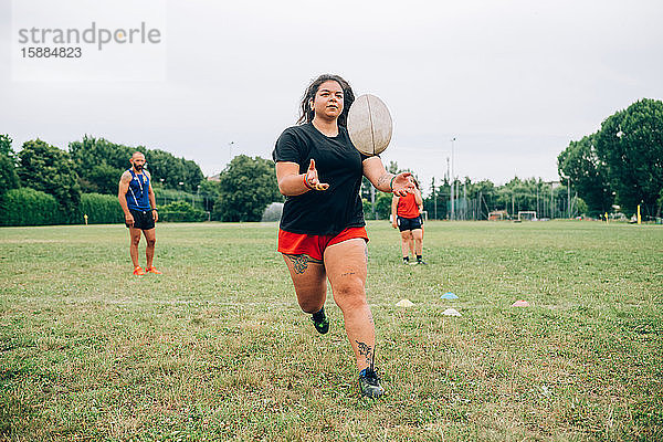 Rugby-Training  Frau fängt einen Rugby-Ball  während andere hinter ihr warten und der Trainer zur Seite steht.
