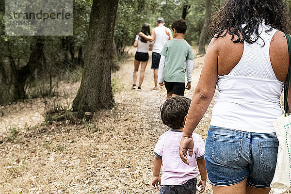 Rückansicht einer Familie mit drei Kindern auf einem Waldweg.