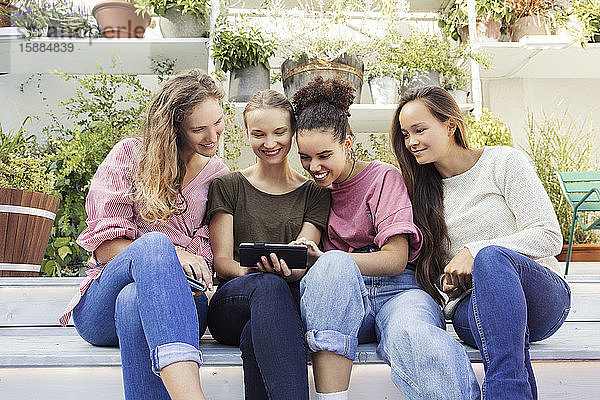 Vier Frauen sitzen in einem Innenhof  schauen auf ein Telefon und lächeln.