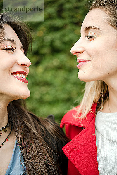 Kopf und Schultern von zwei Frauen im Profil  die sich gegenseitig anschauen und lächeln.