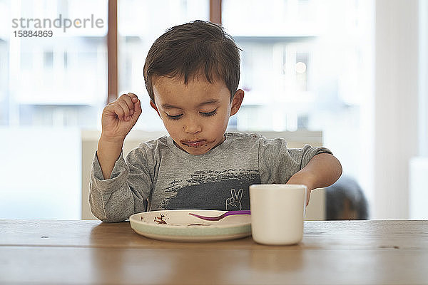 Ein Junge sitzt an einem Tisch und füttert sich mit einer Gabel von einem Teller.