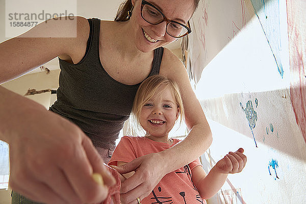 Lächelnde Frau und Mädchen im Haus während der Corona-Virus-Krise  beim Fingermalen.