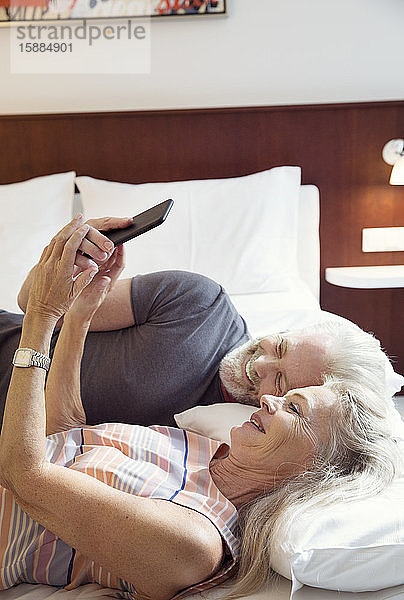 Ein Paar  das auf einem Bett liegt und auf ein Mobiltelefon schaut.