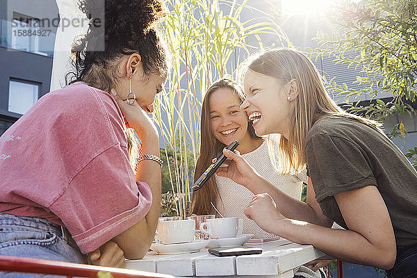 Drei Frauen sitzen um einen Tisch herum  schauen auf ein Mobiltelefon und lächeln.