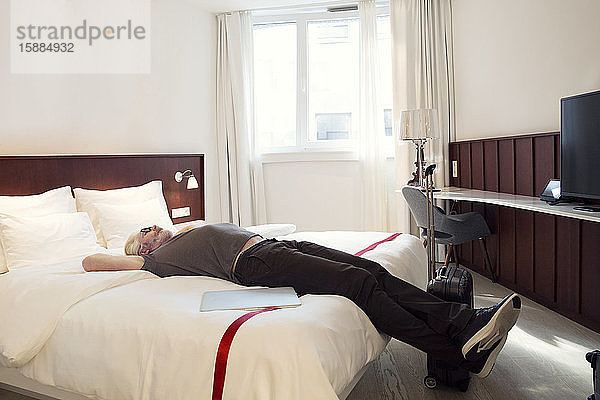 Ein Mann liegt auf einem Bett mit Armen hinter dem Kopf und schaut an die Decke.