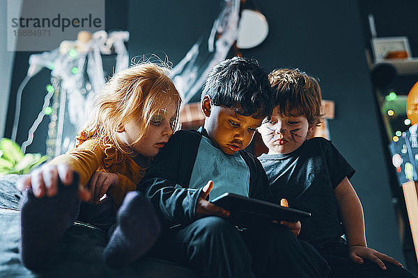 Drei Kinder sitzen auf einem Sitzsack und schauen auf ein Computertablett.