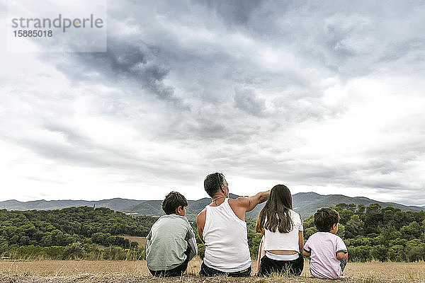 Rückansicht einer Familie mit zwei Kindern in der Landschaft sitzend  in der Ferne die Berge.