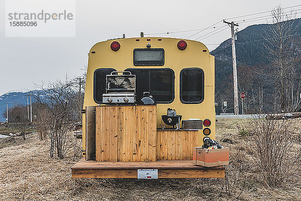Rückansicht eines Wohnmobils mit einem Holzdeck  das für ein Barbecue in einer winterlichen  ländlichen Landschaft eingerichtet ist.