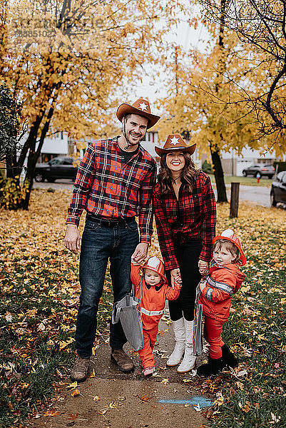 Eine Familie mit zwei Kindern  die für Halloween als Feuerwehrmänner verkleidet sind  posieren für ein Foto in einem mit Blättern übersäten Park.