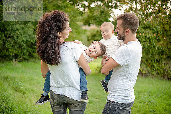 Porträt einer Familie mit zwei Kindern  die auf einer Wiese stehen  lächeln und sich umarmen.