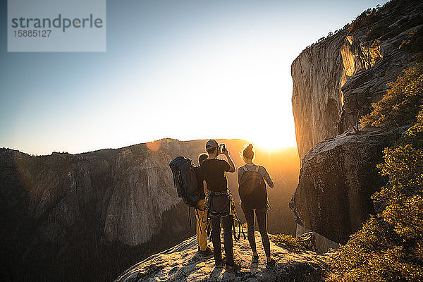 Eine Gruppe von Menschen steht auf einem Felsen und fotografiert einen Sonnenuntergang.
