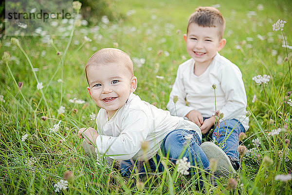 Porträt von zwei Jungen  die auf einer Wiese sitzen und in die Kamera lächeln.