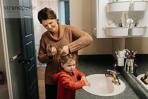 Eine Frau bürstet ihren Töchtern die Haare  während sie im Badezimmer steht.