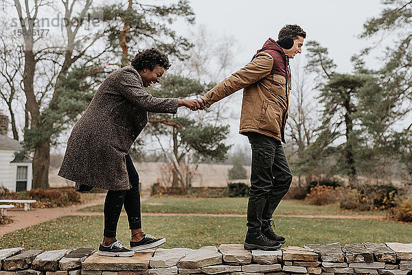 Ein weißer Mann hält Hand in Hand mit einer schwarzen Frau  während sie oben an einer Mauer in einem Garten entlanggehen.