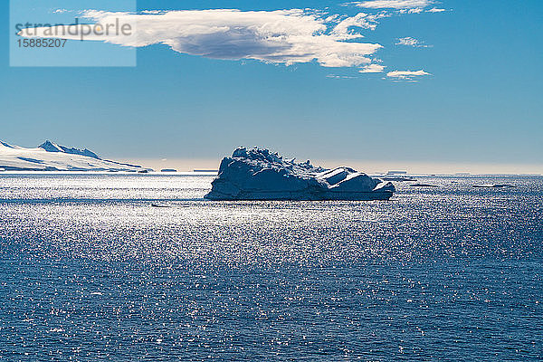 Ein Eisberg  der im südlichen Atlantik unter einem blauen Himmel mit einer Wolke treibt.