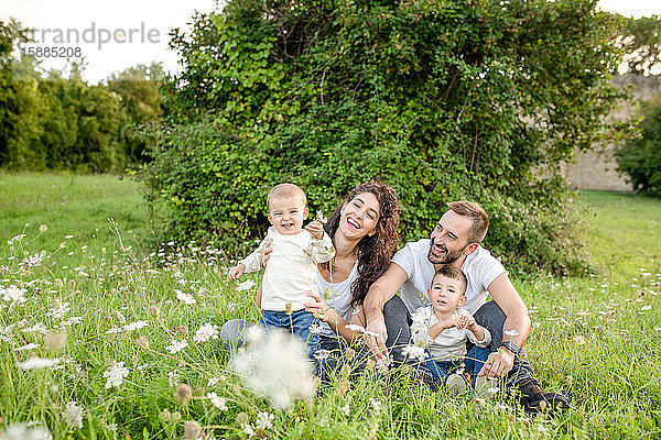 Porträt einer Familie mit zwei Kindern  die auf einer Wiese sitzen und in die Kamera lächeln.