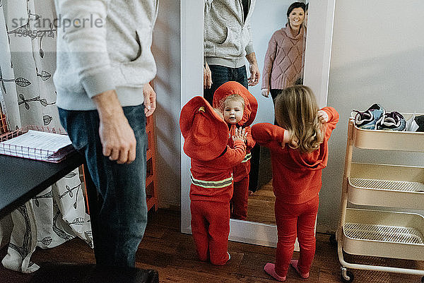 Zwei Kinder  die sich mit ihren Halloween-Kostümen im Spiegel betrachten  während ihre Mutter und ihr Vater zuschauen.