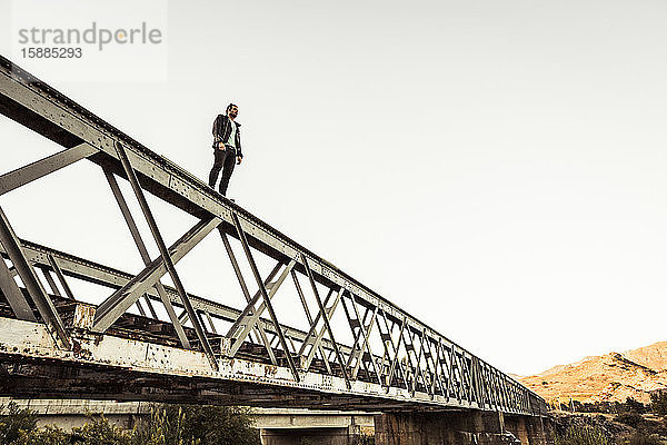 Mann steht auf der Metallstange einer alten Eisenbahnbrücke