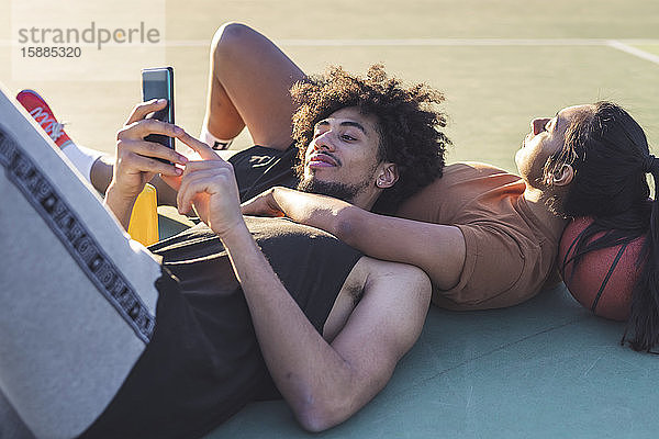 Sportliches junges Paar macht Pause auf Basketballfeld liegend