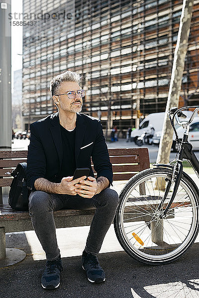 Grauhaariger Geschäftsmann  der in der Stadt auf einer Bank neben dem Fahrrad sitzt