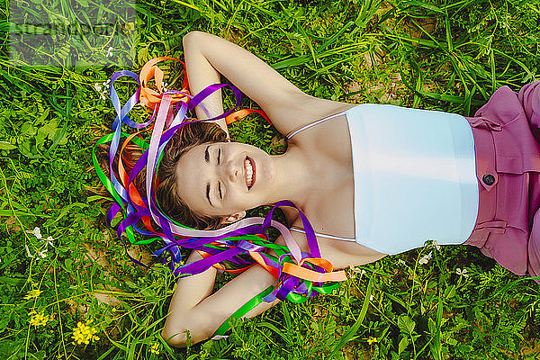 Glückliche junge Frau mit bunten Bändern auf einer Wiese liegend