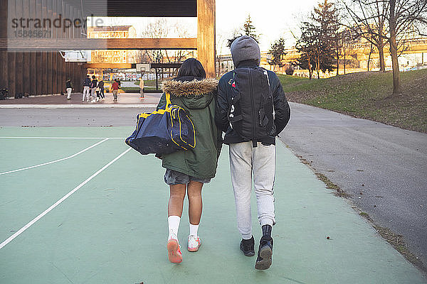 Rückansicht eines jungen Paares beim Gehen auf dem Sportplatz