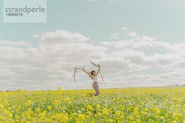 Glückliche junge Frau bewegt sich im Frühling mit bunten Bändern auf einer Blumenwiese