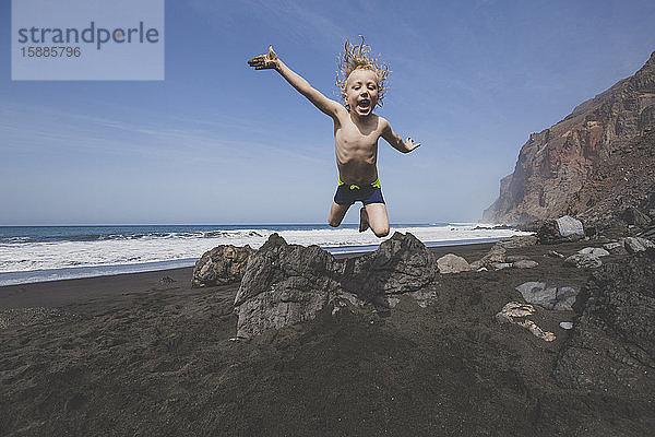 Kleiner Junge springt vor Freude an einem felsigen Strand