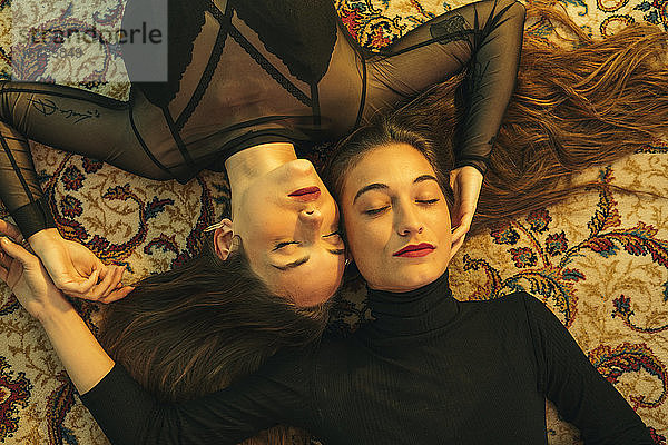 Porträt von zwei jungen Frauen  die Kopf an Kopf auf dem Boden liegen