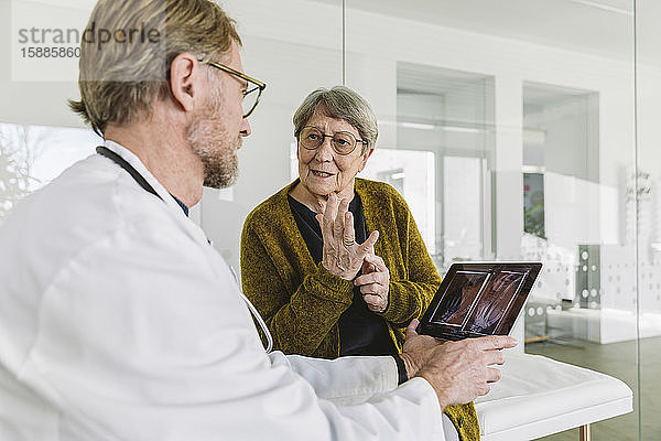 Arzt bespricht Röntgenbild einer gebrochenen Hand mit älterem Patienten