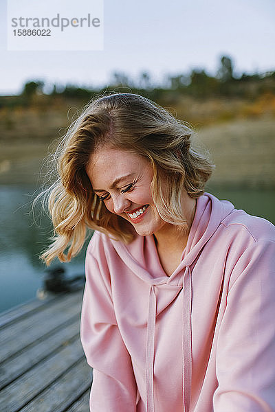 Porträt einer jungen lachenden Frau mit rosa Kapuzenpullover auf dem Steg