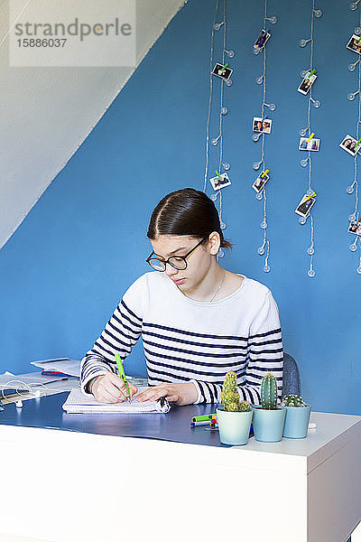 Porträt eines Mädchens  das zu Hause am Schreibtisch sitzt und Hausaufgaben macht