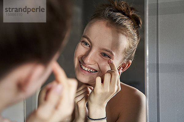Spiegelbild eines lachenden Mädchens  das im Badezimmer Gesichtscreme aufträgt