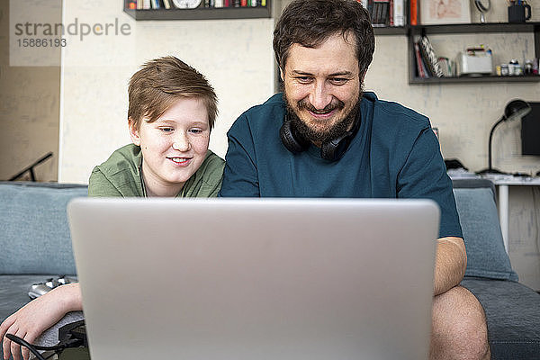 Porträt von Vater und Sohn  die zusammen auf der Couch sitzen und einen Laptop benutzen
