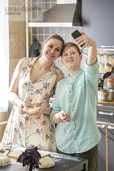 Mutter und Sohn beim Selbermachen mit Smartphone in der Küche