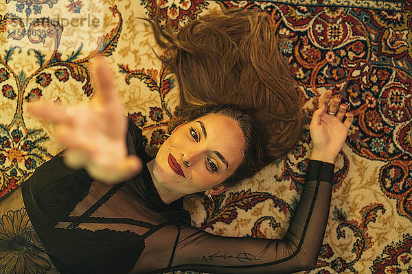 Porträt einer tätowierten jungen Frau  die auf dem Boden liegt und ihre Hand hebt