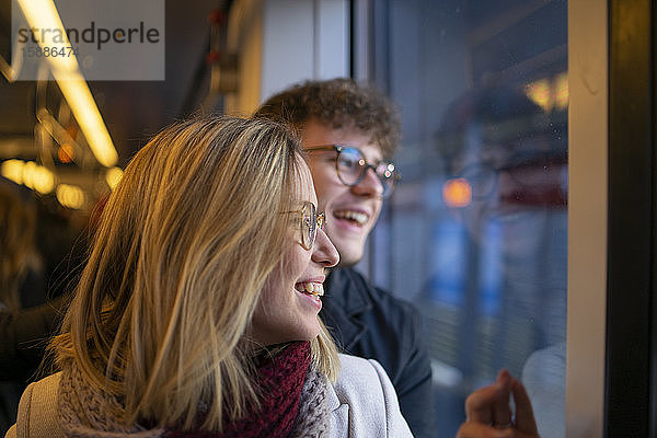 Lachende junge Frau  die mit ihrem Freund in der Straßenbahn sitzt und aus dem Fenster schaut