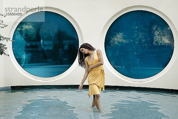 Junge Frau in gelbem Sommerkleid tanzt im Pool