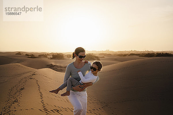 Mutter trägt Tochter in Sanddünen bei Sonnenuntergang  Gran Canaria  Spanien