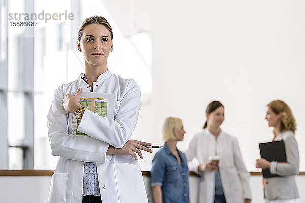 Porträt einer Ärztin im Krankenhaus mit Kollegen im Hintergrund