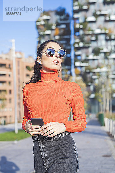 Schöne Frau mit Sonnenbrille und Smartphone in der Hand in der Stadt