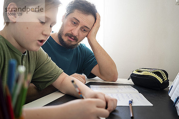 Porträt eines Vaters  der seinen Sohn bei den Hausaufgaben beobachtet
