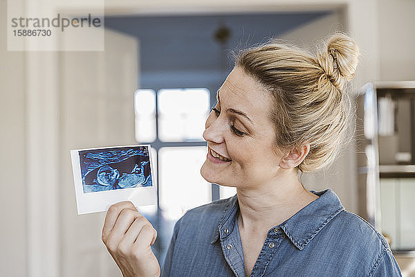 Schwangere Frau hält Ultraschallbild zu Hause
